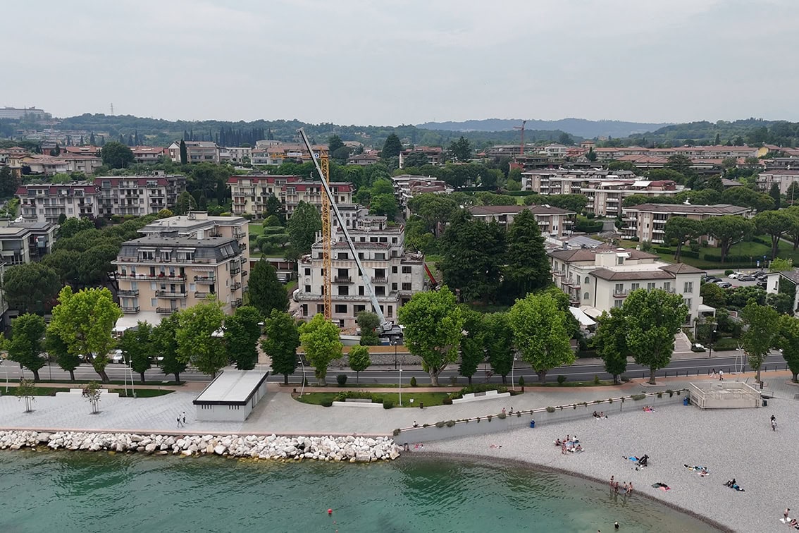 Vista frontale dal litorale della costruzione Villa Olympia Residences a Desenzano del Garda, evidenziando la posizione fronte lago del progetto.;