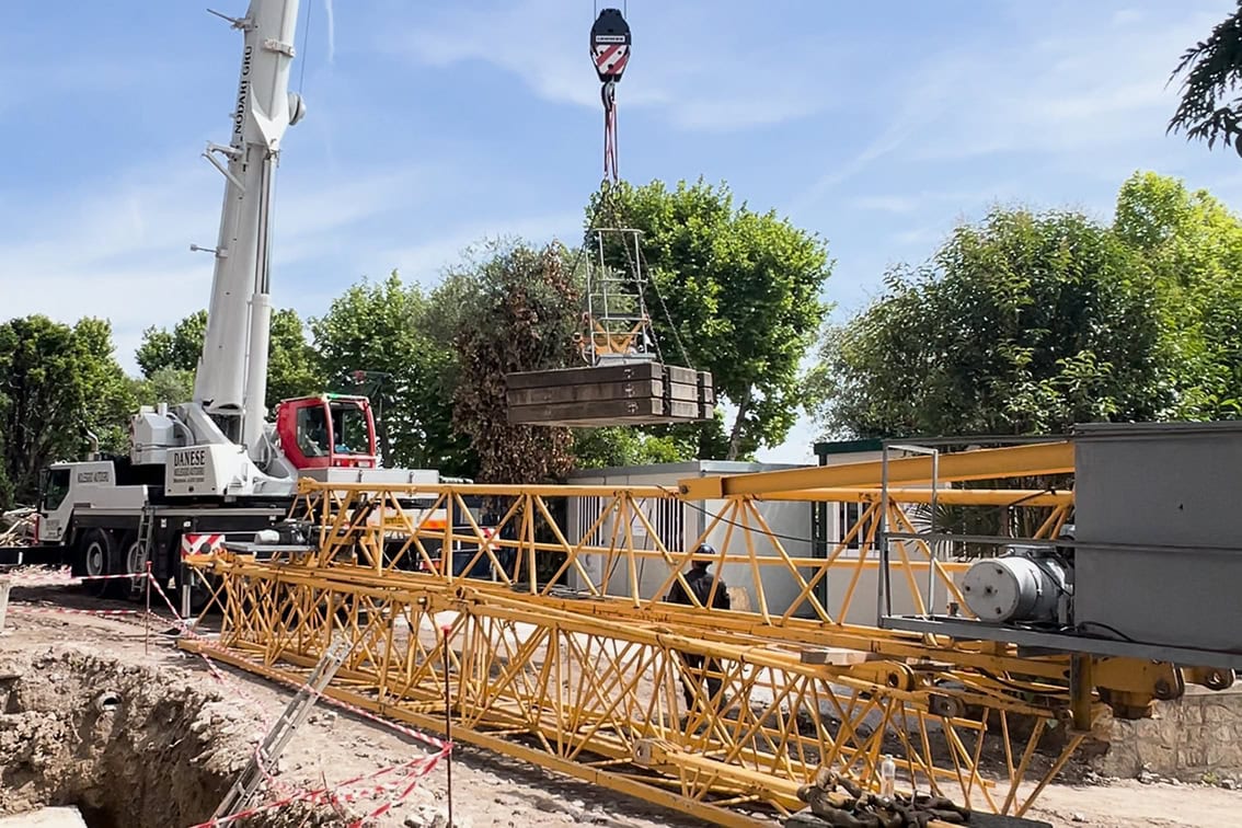 Una gru solleva un carico pesante sopra l'area di cantiere di Villa Olympia Residences, fase di montaggio finale della macchina operatrice.;